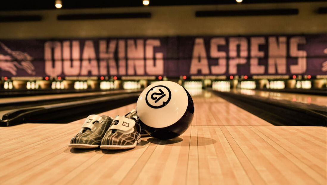 Photo of bowling shoes, bowling ball, in front of a bowling lane. Above the lane reads 
